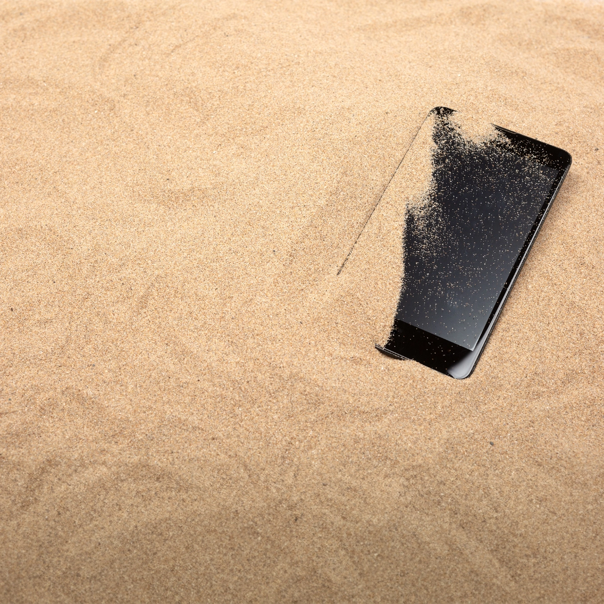 A photo of a mobile phone partially covered in sand on a beach